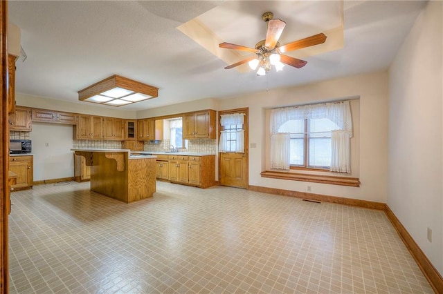 kitchen featuring sink, a breakfast bar area, a center island, ceiling fan, and decorative backsplash