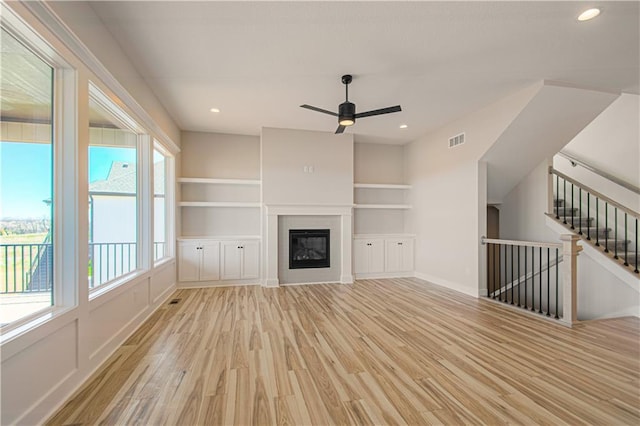 unfurnished living room with built in shelves, light wood-style flooring, recessed lighting, visible vents, and a glass covered fireplace