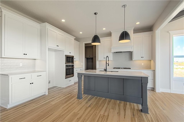 kitchen with a kitchen island with sink, light countertops, stainless steel oven, and white cabinetry