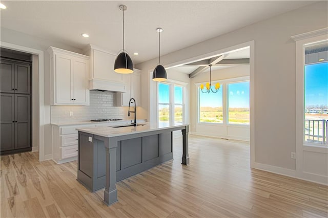 kitchen featuring white cabinets, a sink, backsplash, and an island with sink