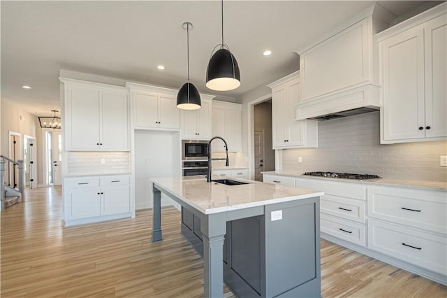 kitchen featuring a kitchen island with sink, a sink, white cabinets, appliances with stainless steel finishes, and pendant lighting