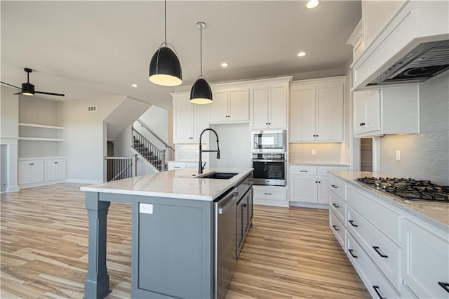 kitchen with appliances with stainless steel finishes, white cabinets, premium range hood, and a center island with sink