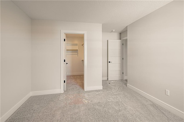 unfurnished bedroom with light carpet, a spacious closet, baseboards, and a textured ceiling