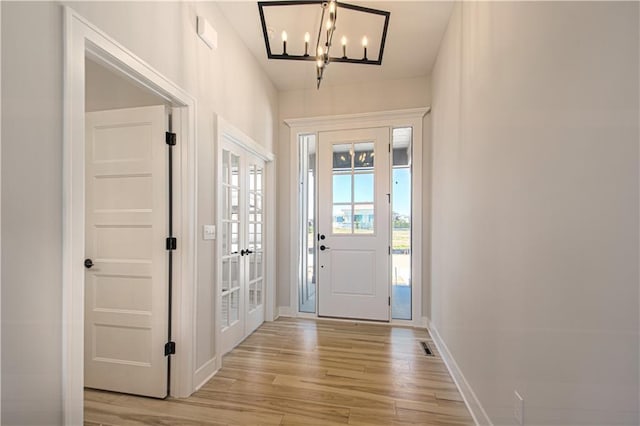 foyer entrance featuring light wood-style floors, baseboards, a notable chandelier, and french doors