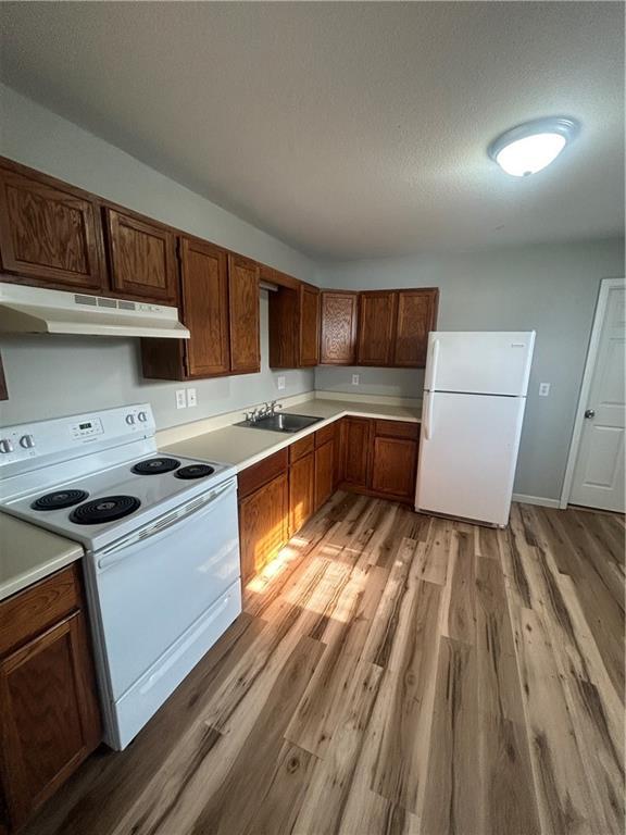 kitchen featuring a textured ceiling, light hardwood / wood-style flooring, white appliances, and sink