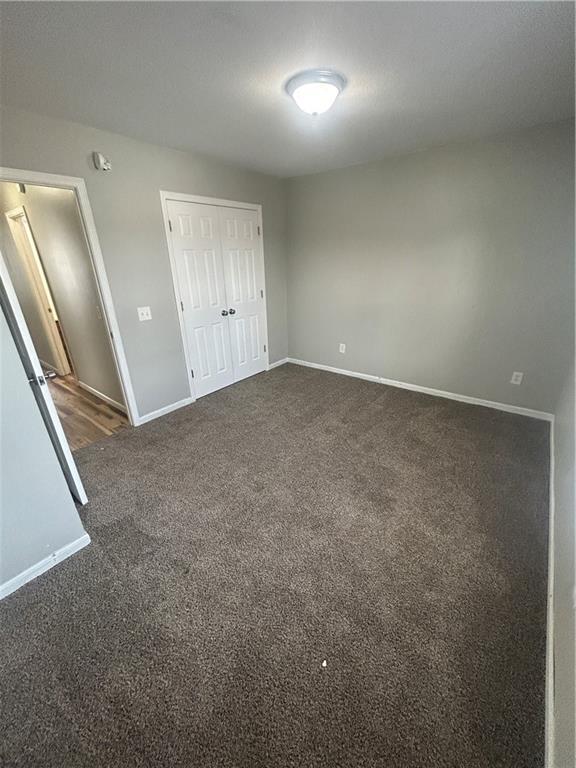 unfurnished bedroom with dark carpet and a closet