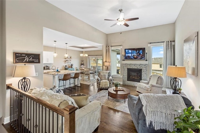 living room with dark hardwood / wood-style floors, a stone fireplace, plenty of natural light, and ceiling fan with notable chandelier