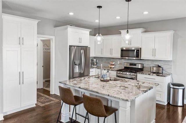 kitchen with stainless steel appliances, white cabinetry, a kitchen island with sink, and pendant lighting