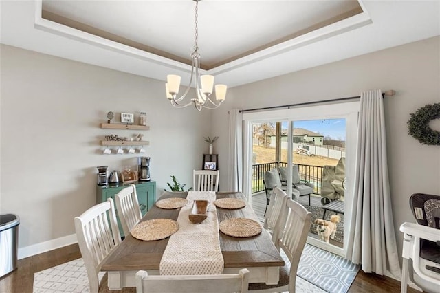 dining area featuring a raised ceiling, dark hardwood / wood-style flooring, and an inviting chandelier