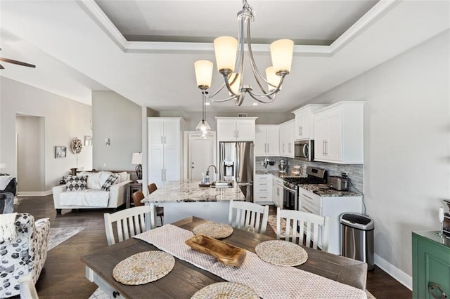 dining room featuring ceiling fan with notable chandelier, sink, a tray ceiling, and dark hardwood / wood-style floors