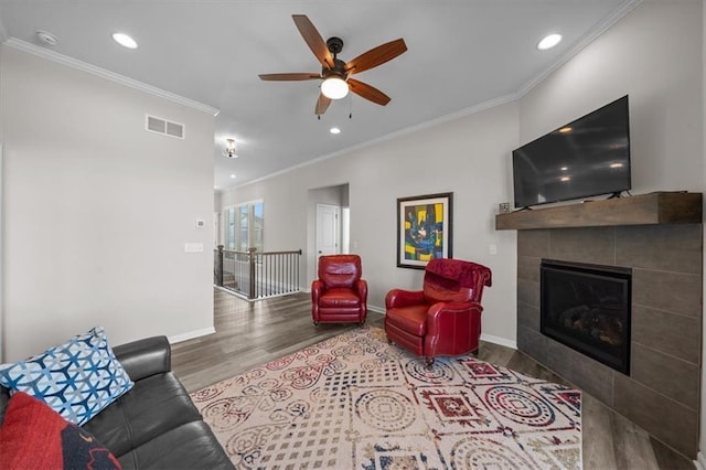 living room with hardwood / wood-style floors, a fireplace, ornamental molding, and ceiling fan