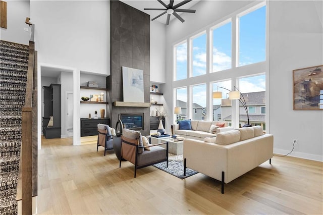 living room featuring a tiled fireplace, ceiling fan, light hardwood / wood-style flooring, and a high ceiling