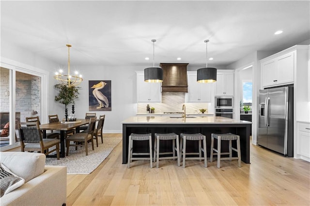 kitchen with white cabinetry, stainless steel appliances, an island with sink, pendant lighting, and custom range hood