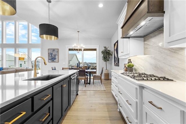 kitchen with tasteful backsplash, custom range hood, sink, white cabinetry, and hanging light fixtures