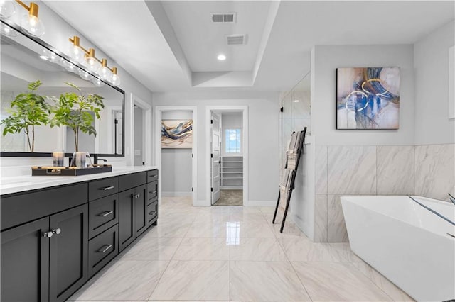 bathroom featuring vanity, a tub to relax in, a tray ceiling, and tile walls