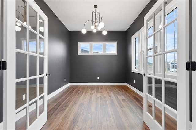 unfurnished room featuring an inviting chandelier, french doors, baseboards, and wood finished floors