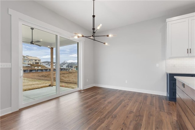 unfurnished dining area featuring a notable chandelier, dark wood-type flooring, and baseboards