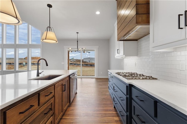 kitchen with brown cabinetry, appliances with stainless steel finishes, hanging light fixtures, premium range hood, and a sink