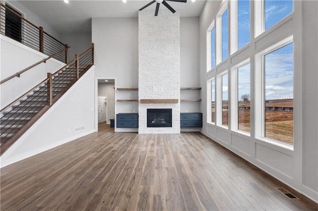 unfurnished living room with a fireplace, wood finished floors, visible vents, a ceiling fan, and stairway