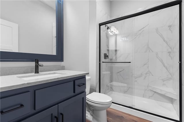 bathroom featuring vanity, wood finished floors, a marble finish shower, and toilet