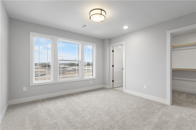 unfurnished bedroom featuring recessed lighting, light carpet, visible vents, baseboards, and a spacious closet