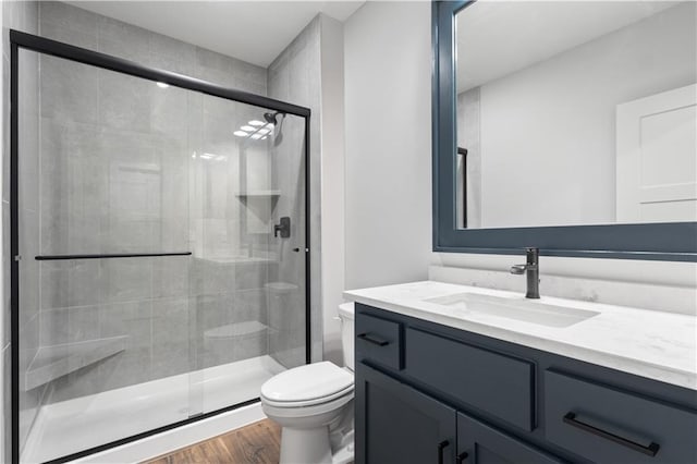 full bath featuring wood finished floors, a shower stall, toilet, and vanity