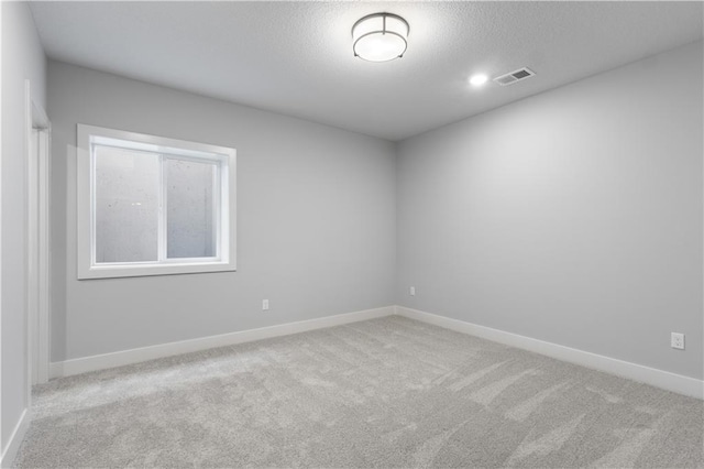 empty room with light carpet, a textured ceiling, visible vents, and baseboards