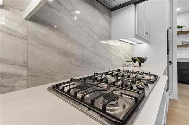 details with light wood-style flooring, backsplash, white cabinetry, stainless steel gas stovetop, and light countertops