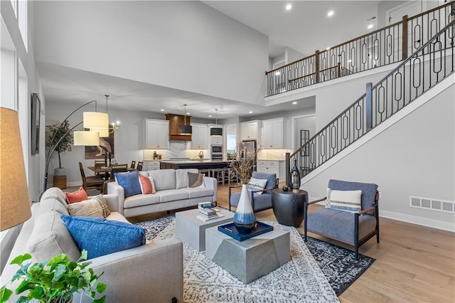 living area with stairway, baseboards, visible vents, a high ceiling, and light wood-style flooring