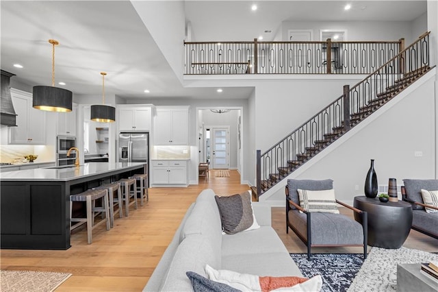 living area with a towering ceiling, recessed lighting, light wood-style flooring, and stairs