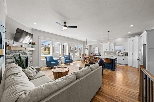 living room featuring ceiling fan with notable chandelier, a fireplace, light hardwood / wood-style floors, crown molding, and a textured ceiling