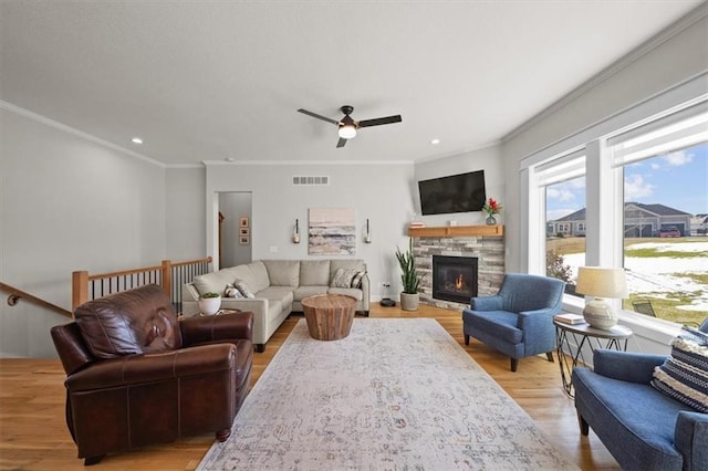 living room featuring ceiling fan, ornamental molding, a stone fireplace, and light hardwood / wood-style flooring