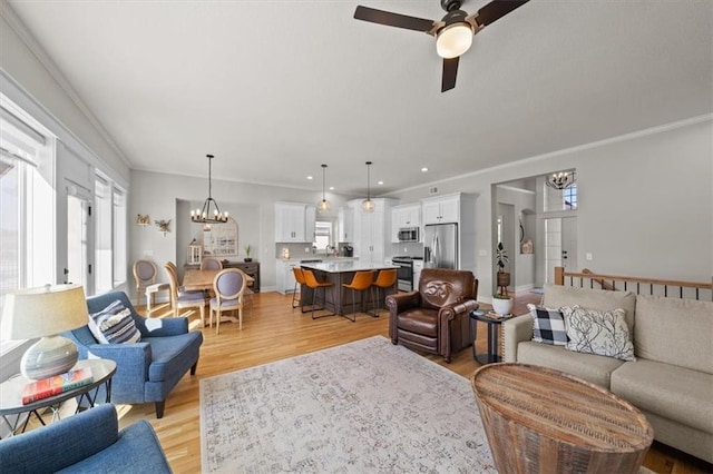 living room with crown molding, ceiling fan with notable chandelier, and light hardwood / wood-style flooring