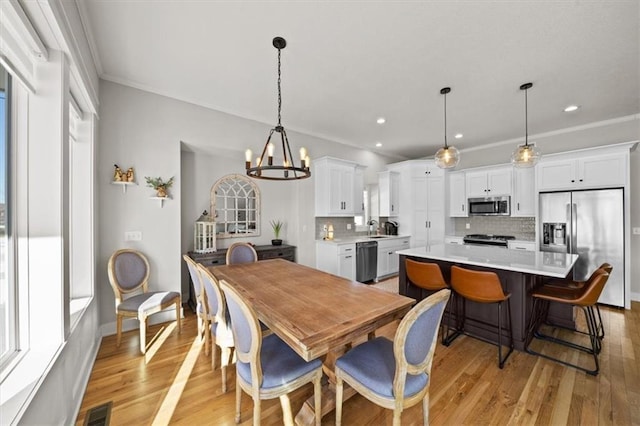 dining area featuring an inviting chandelier, sink, ornamental molding, and light wood-type flooring