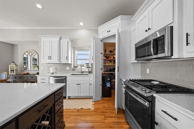 kitchen with appliances with stainless steel finishes, tasteful backsplash, sink, white cabinets, and light hardwood / wood-style flooring