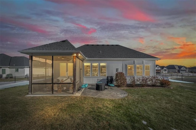 back house at dusk with a yard, a patio area, and a sunroom