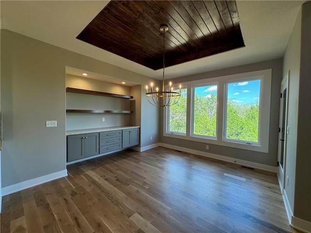 unfurnished dining area featuring hardwood / wood-style floors, a tray ceiling, an inviting chandelier, and wooden ceiling