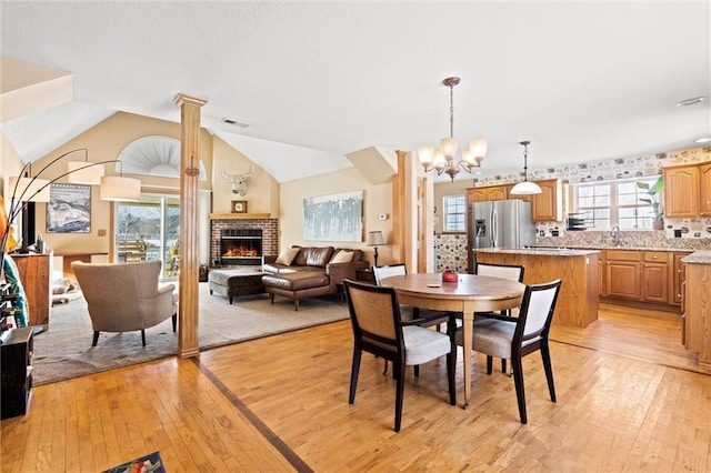 dining space with a chandelier, ornate columns, a fireplace, light hardwood / wood-style flooring, and lofted ceiling