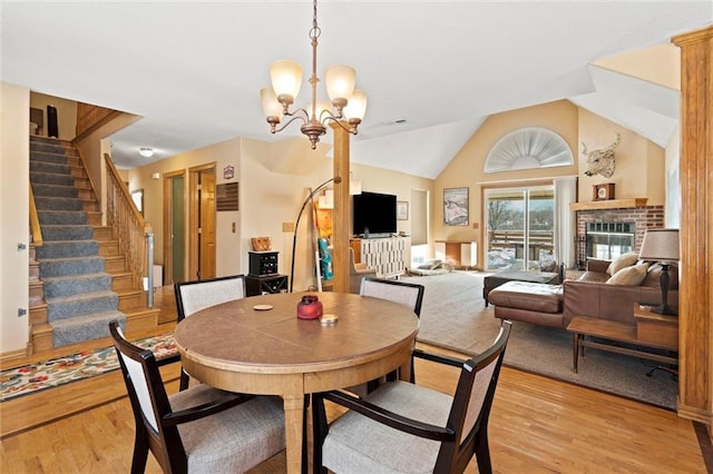 dining room with a notable chandelier, light hardwood / wood-style flooring, a brick fireplace, and vaulted ceiling