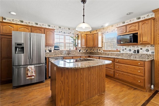 kitchen with light stone counters, light hardwood / wood-style flooring, hanging light fixtures, black appliances, and a kitchen island