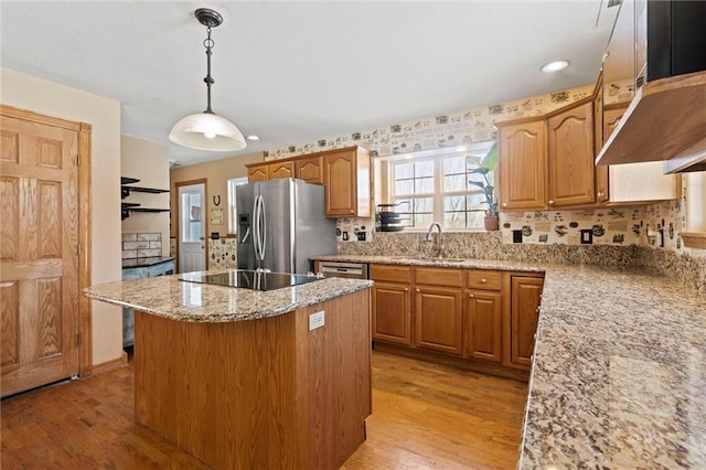 kitchen with appliances with stainless steel finishes, hanging light fixtures, a kitchen island, sink, and light hardwood / wood-style flooring