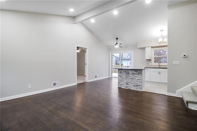 unfurnished living room featuring ceiling fan with notable chandelier, lofted ceiling with beams, dark wood-type flooring, and sink