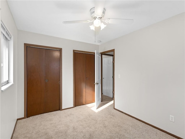 unfurnished bedroom featuring ceiling fan, light carpet, and multiple closets