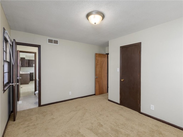 unfurnished bedroom featuring light carpet, ensuite bathroom, and a textured ceiling