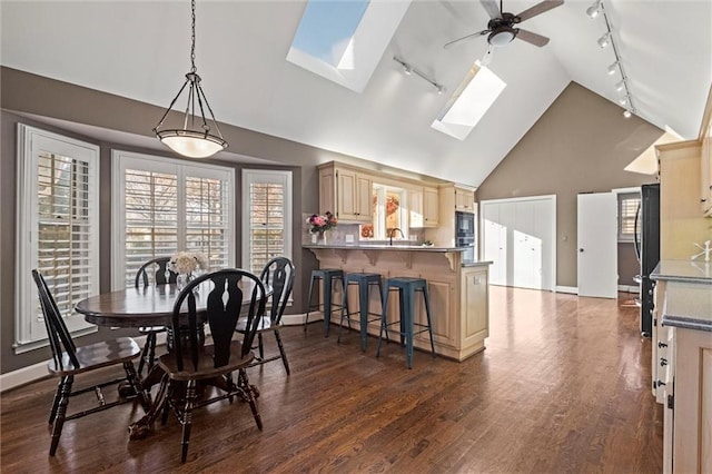 dining area with ceiling fan, a skylight, dark wood-type flooring, and high vaulted ceiling