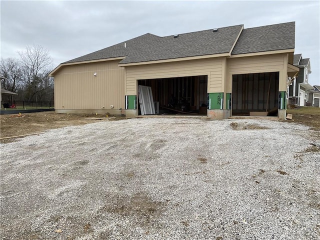 view of property exterior with a shingled roof and gravel driveway