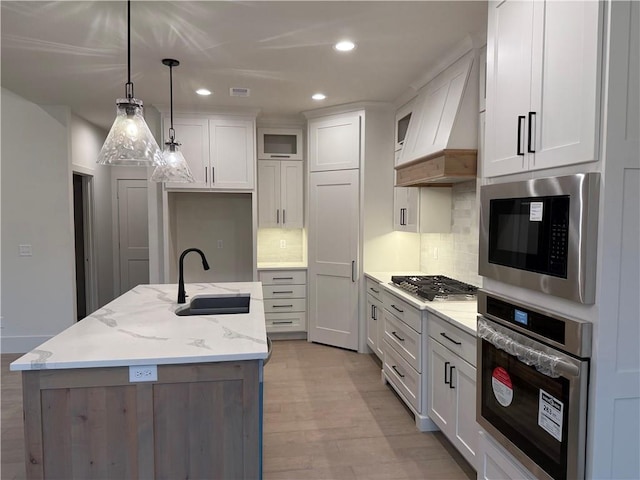9301 SW Leviathan Ct, Lees Summit, MO 64064 - kitchen with stainless steel appliances, a sink, custom exhaust hood, light wood finished floors, and a kitchen island with sink