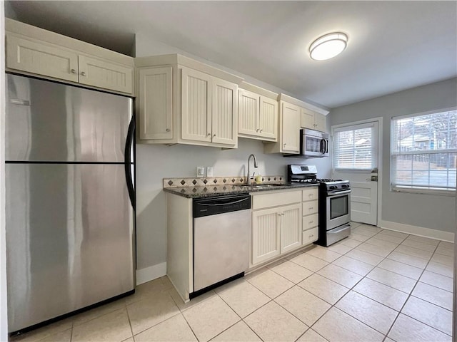 kitchen with sink, stainless steel appliances, dark stone countertops, cream cabinetry, and light tile patterned flooring