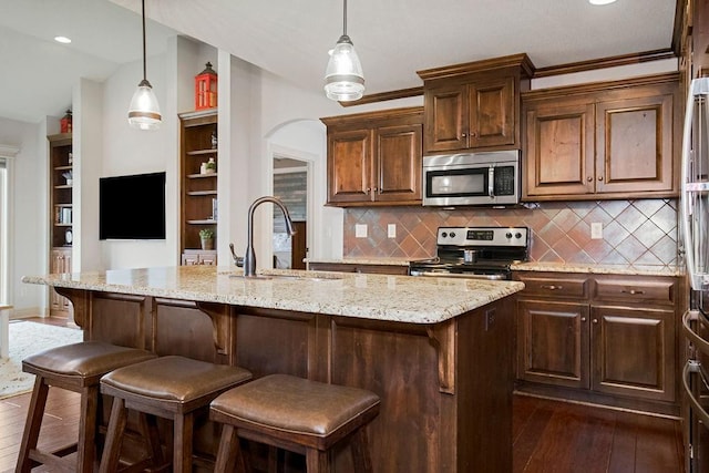 kitchen with sink, stainless steel appliances, dark hardwood / wood-style floors, a breakfast bar, and a center island with sink