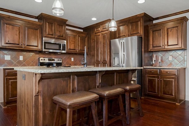 kitchen featuring dark hardwood / wood-style flooring, ornamental molding, stainless steel appliances, pendant lighting, and an island with sink